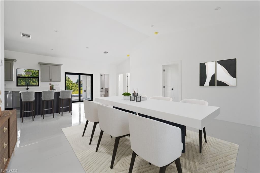 Spacious dining area with vaulted ceilings, tile flooring, and a kitchen featuring gray cabinetry, a breakfast bar, and sliding glass doors