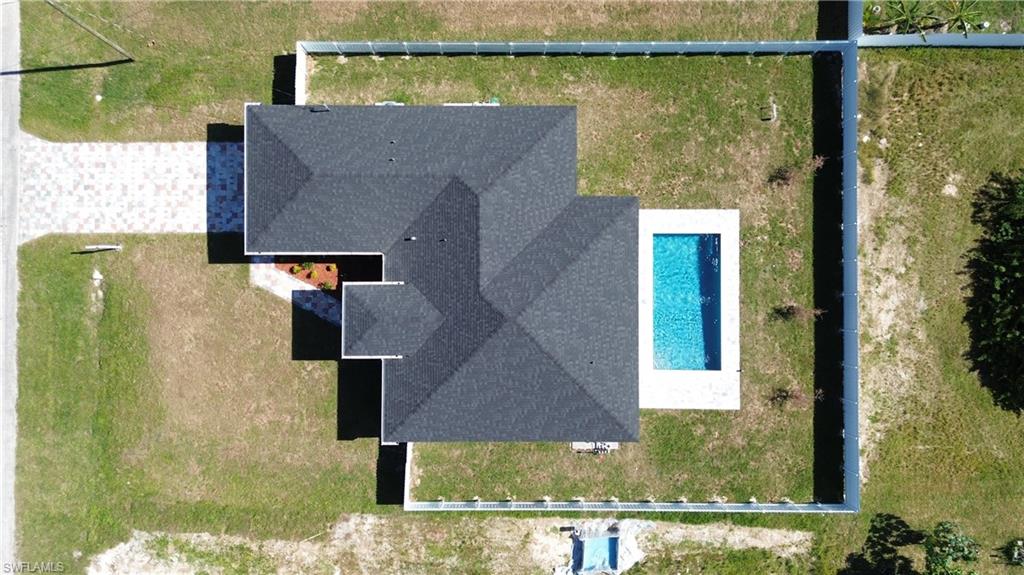 Paved driveway, dark shingle roof, rectangular swimming pool with surrounding deck, privacy fencing, and green lawn