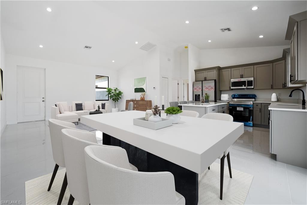 Open-concept living area featuring high vaulted ceilings, recessed lighting, tile flooring, a kitchen with gray cabinetry, and a central island with countertop seating