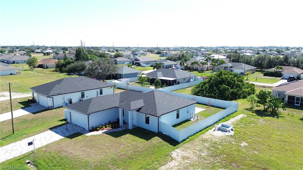 New construction residence featuring a white exterior, dark shingle roof, paved driveway, and a white privacy fence