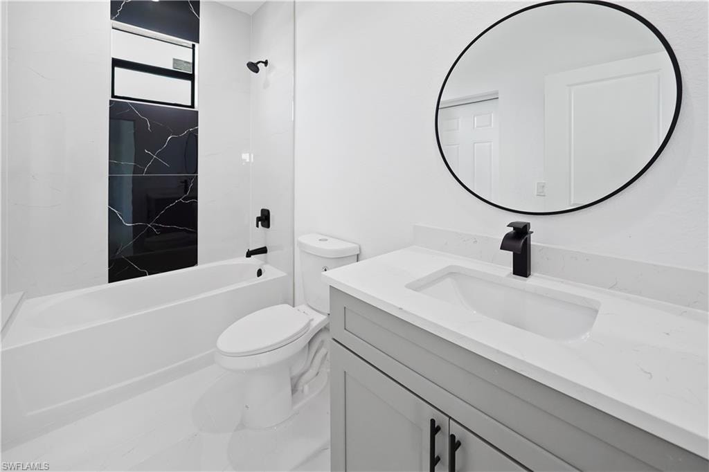Modern bathroom featuring a white bathtub, black marble-patterned tile, a gray vanity with an integrated sink, a round mirror, and matte black fixtures