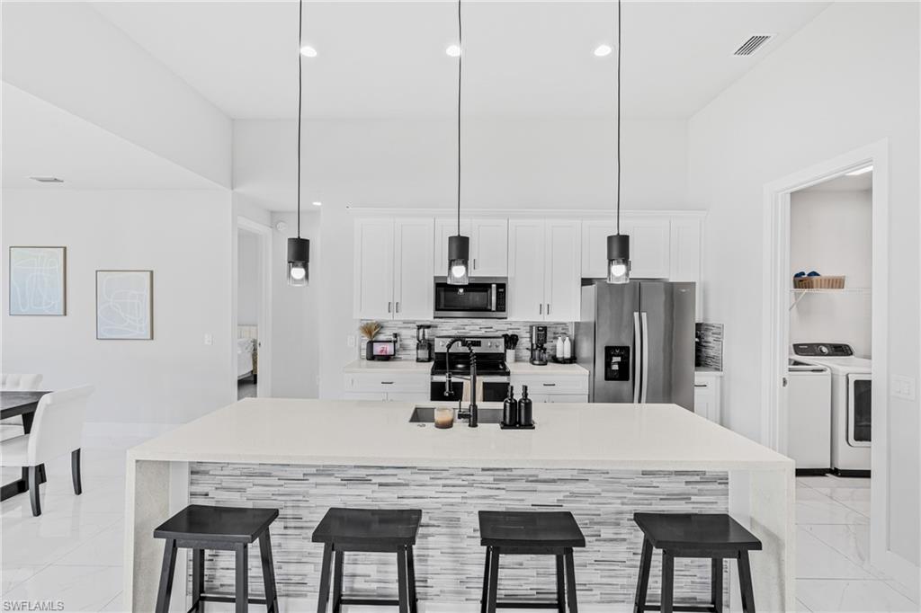 Kitchen with a large island featuring pendant lighting, integrated sink, and a tiled accent panel