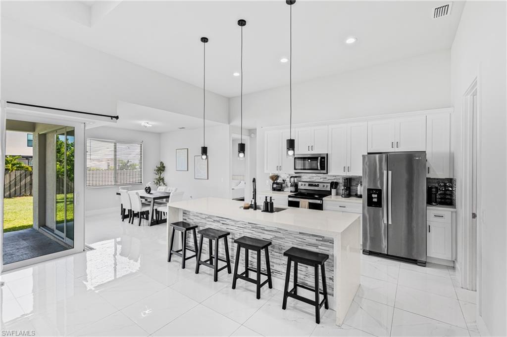 Spacious kitchen and dining area featuring white cabinetry, stainless steel appliances, a kitchen island with pendant lighting, and white tile flooring
