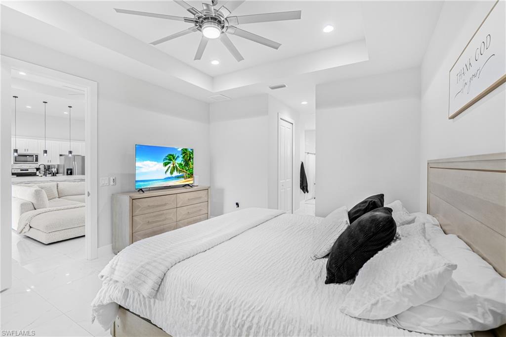 Tray ceiling with recessed lighting, ceiling fan with integrated light, white tile flooring, and a light wood-finish headboard