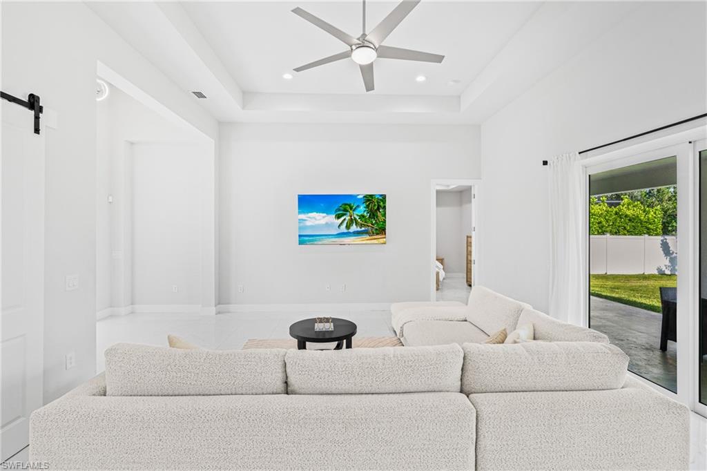 Bright, open-concept living space featuring a neutral-toned sectional arrangement, ceiling fan with brushed-metal finish, recessed lighting throughout, and glass sliding doors opening to outdoor grounds