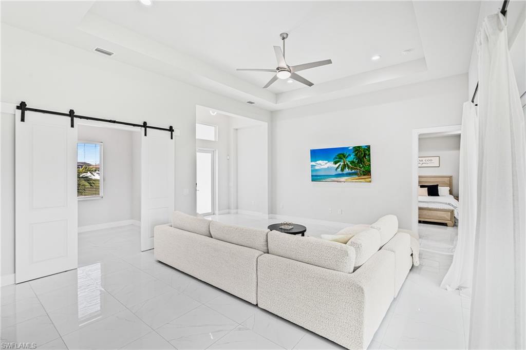 Spacious interior featuring a tray ceiling, recessed lighting, white tile flooring, barn doors, and a ceiling fan