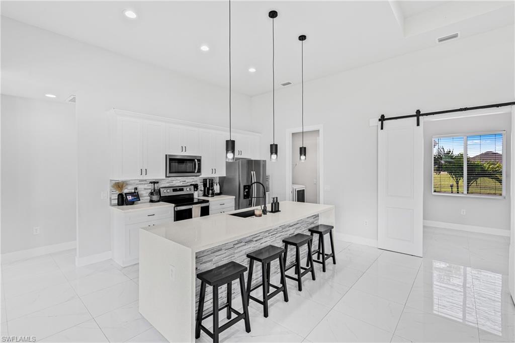 Modern kitchen featuring white cabinetry, a large island with a waterfall countertop, stainless steel appliances, and a tile backsplash