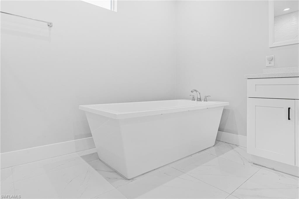Freestanding soaking tub with chrome fixtures, white vanity with black hardware, and large format floor tiling