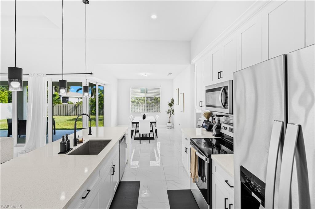 Kitchen island with a built-in sink, white cabinetry, integrated stainless steel appliances, and large format tile flooring