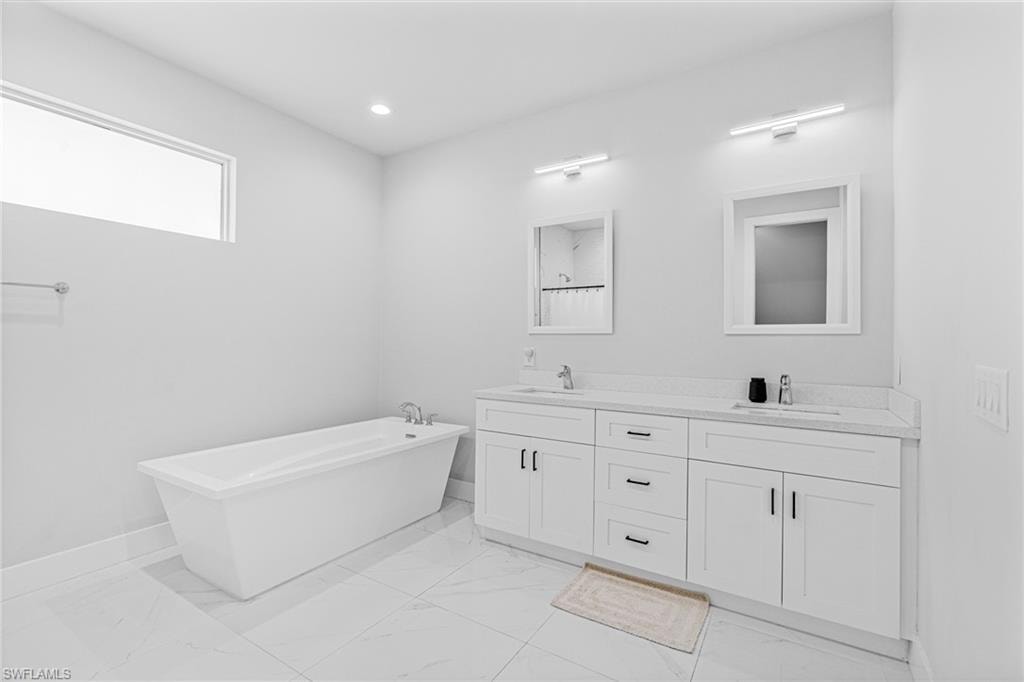 Freestanding soaking tub, dual vanity with white cabinetry, integrated sinks, and polished chrome fixtures