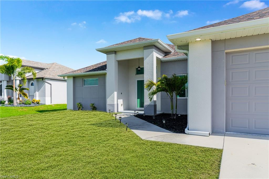 Contemporary stucco exterior with a covered entry, established landscaping, and an attached garage