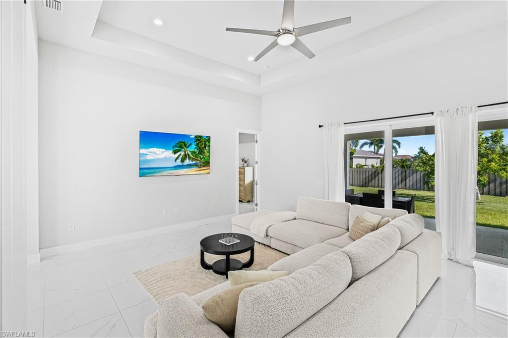 Bright living space featuring white tile flooring, a tray ceiling, and recessed lighting