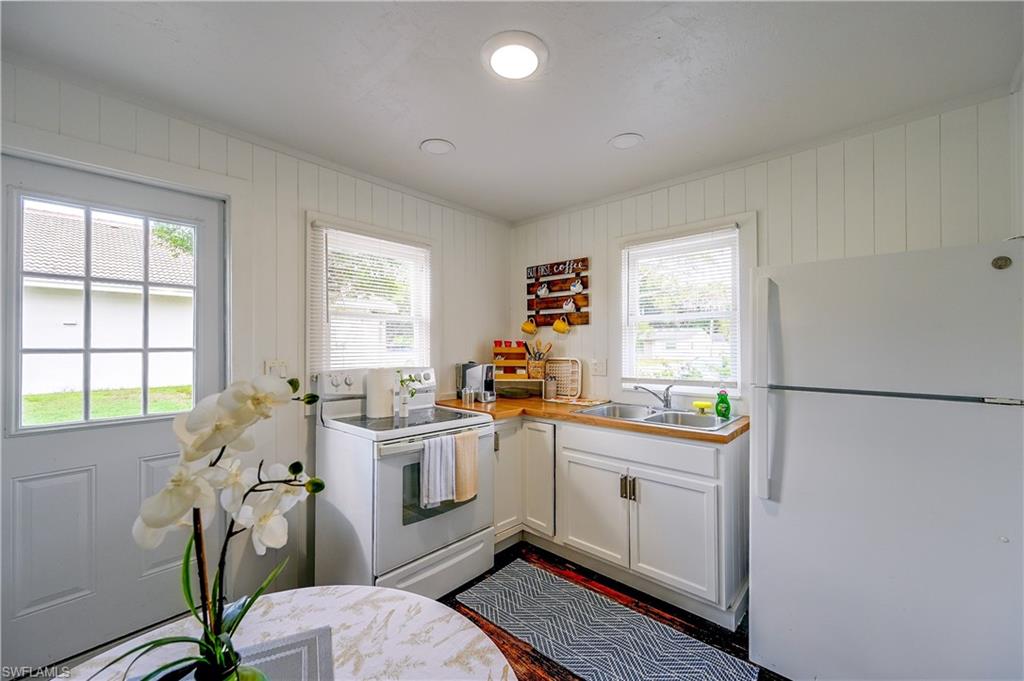 Kitchen featuring white cabinetry, wood-finish countertops, stainless steel sink, and white appliances