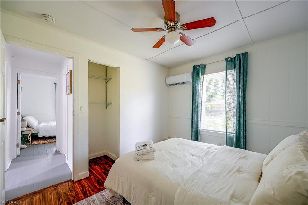 Room featuring a ceiling fan, window with natural light, wall-mounted air conditioning unit, and wood-finish flooring