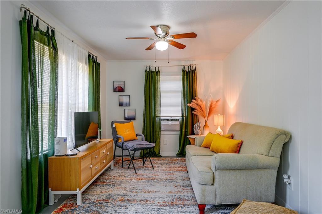 White painted walls, wood-finish ceiling fan with integrated lighting, multiple windows, and a window air conditioning unit