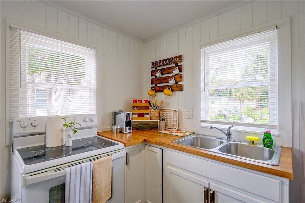 White paneled walls, wood-finish countertops, dual-basin stainless steel sink, and white cabinetry