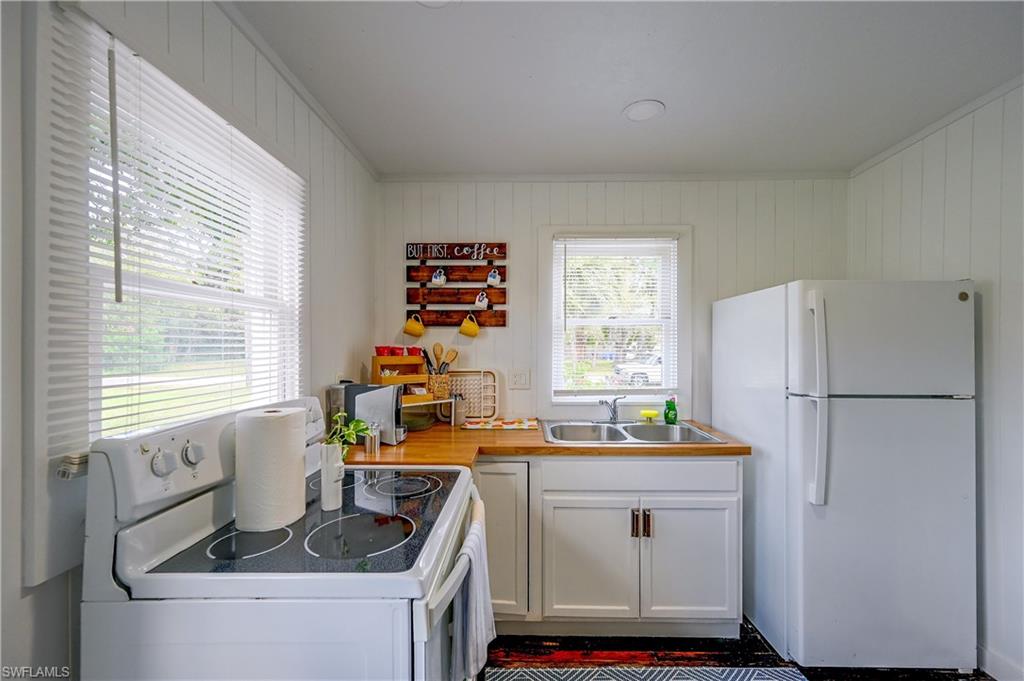 Kitchen featuring wood-finish countertops, white cabinetry, a double basin stainless steel sink, and white appliances