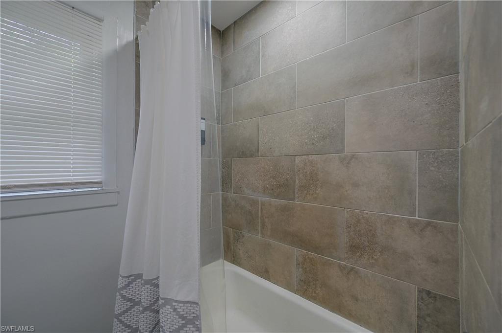 Bathtub with full-height subway tile surround, clear glass shower panel, and a window with blinds