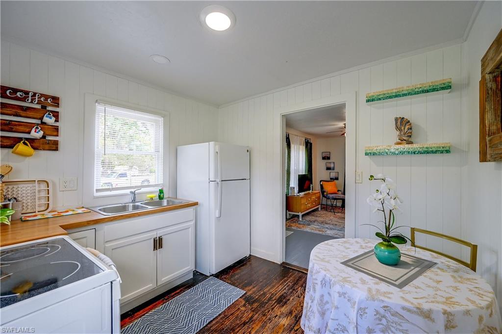 Kitchen featuring wood-finish countertops, white cabinetry with gold-tone hardware, a double-basin stainless steel sink, and wood-finish flooring