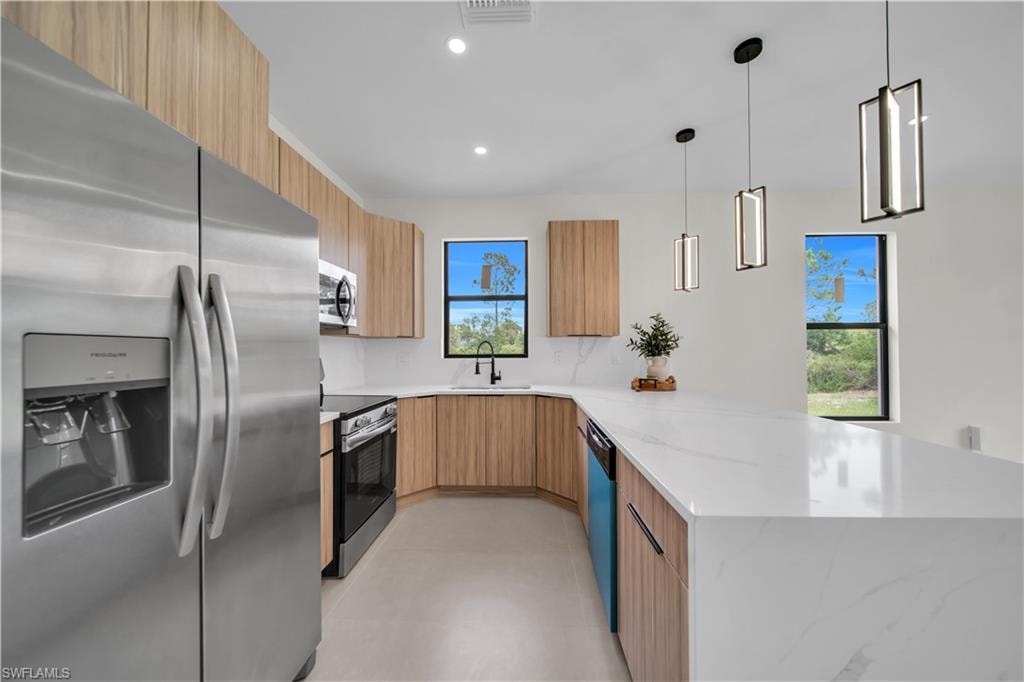 Contemporary kitchen featuring stainless steel appliances, light wood-finish cabinetry, a waterfall-edge island, and pendant lighting fixtures