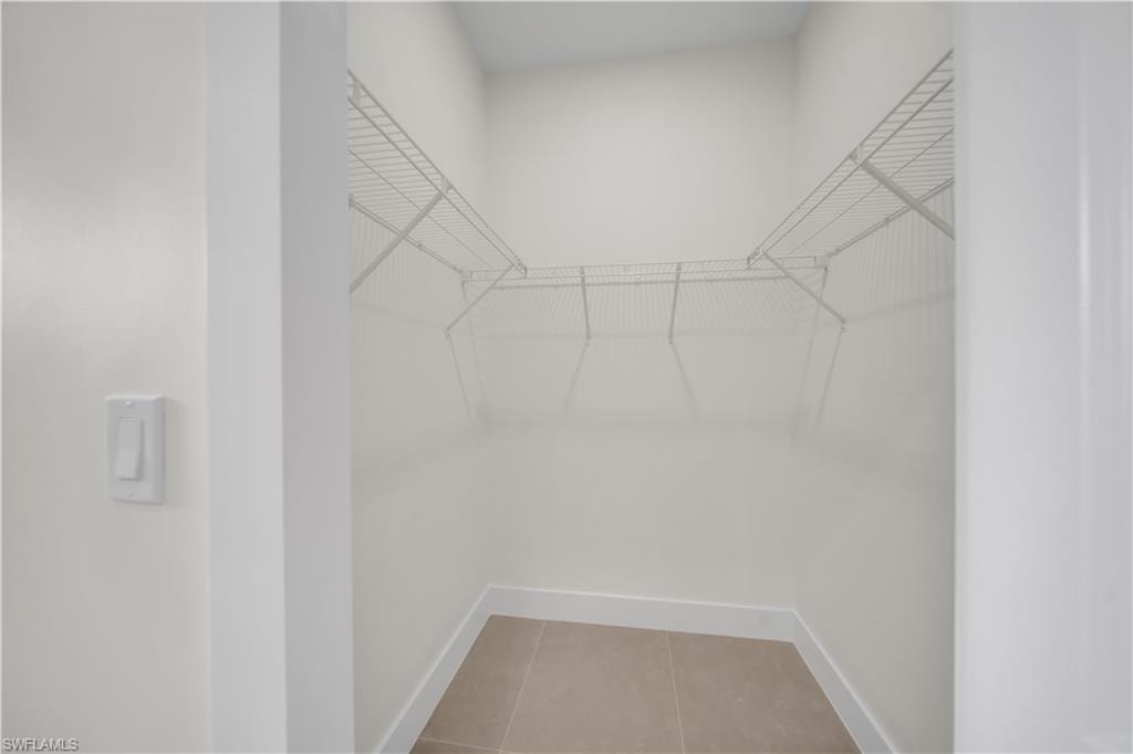 Walk-in closet featuring wire shelving, light-toned tile flooring, and white baseboards
