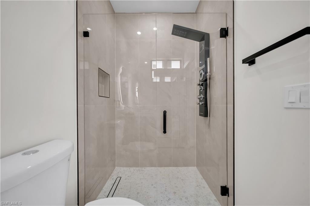 Glass-enclosed shower with a modern shower panel system, integrated niche, and light-toned tile surround