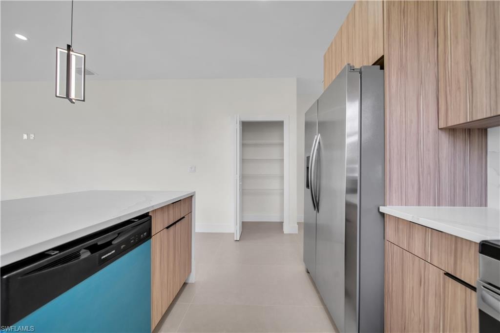 Kitchen featuring wood-finish cabinetry, stainless steel refrigerator, white countertops, and a modern pendant light fixture