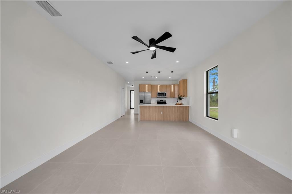 Open-concept living space featuring large format tile flooring, a modern black ceiling fan, recessed lighting, and a kitchen with wood-finish cabinetry and stainless steel appliances