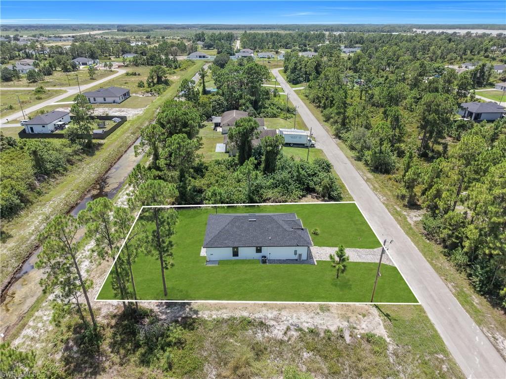 Lush green lawn, paved driveway, mature trees, single-story residence, asphalt shingle roof