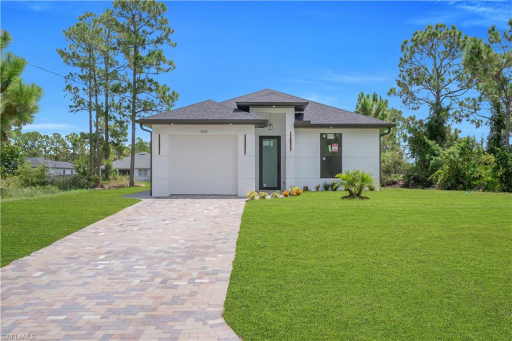 Modern exterior with a light-colored facade, dark shingle roof, and a paver driveway