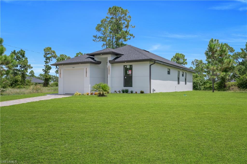 Single-story exterior with a two-car garage, dark shingle roof, white stucco siding, and a paved driveway