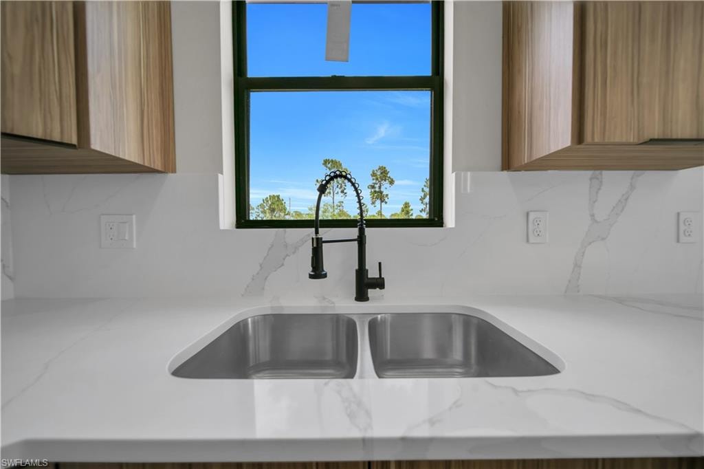 White countertop with integrated dual stainless steel sinks, black gooseneck faucet, full-height backsplash, wood-finish cabinetry, and a black-framed window