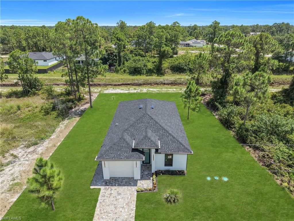 New construction residence featuring a dark shingle roof, light-toned exterior, and a paver driveway