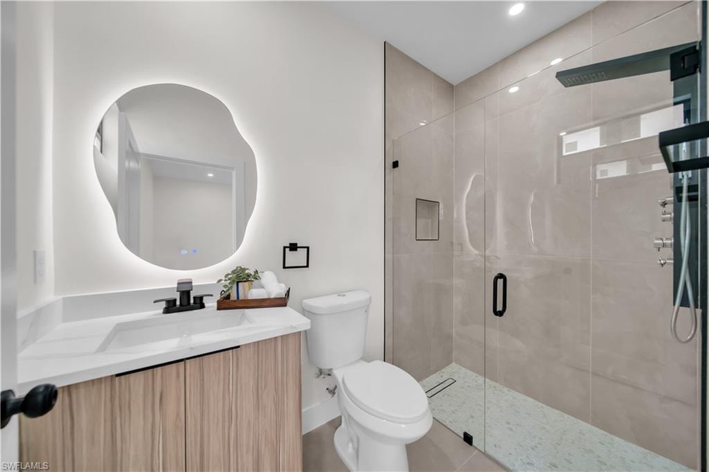 Integrated vanity with a rectangular basin and light wood-finish cabinetry, illuminated mirror with an organic shape, frameless glass shower enclosure, and large format wall tile