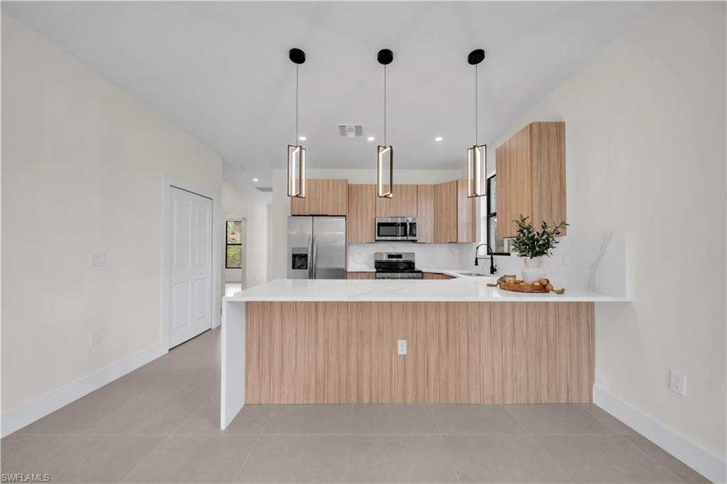 Contemporary kitchen with wood-finish cabinetry, stainless steel appliances, and a white countertop island with pendant lighting