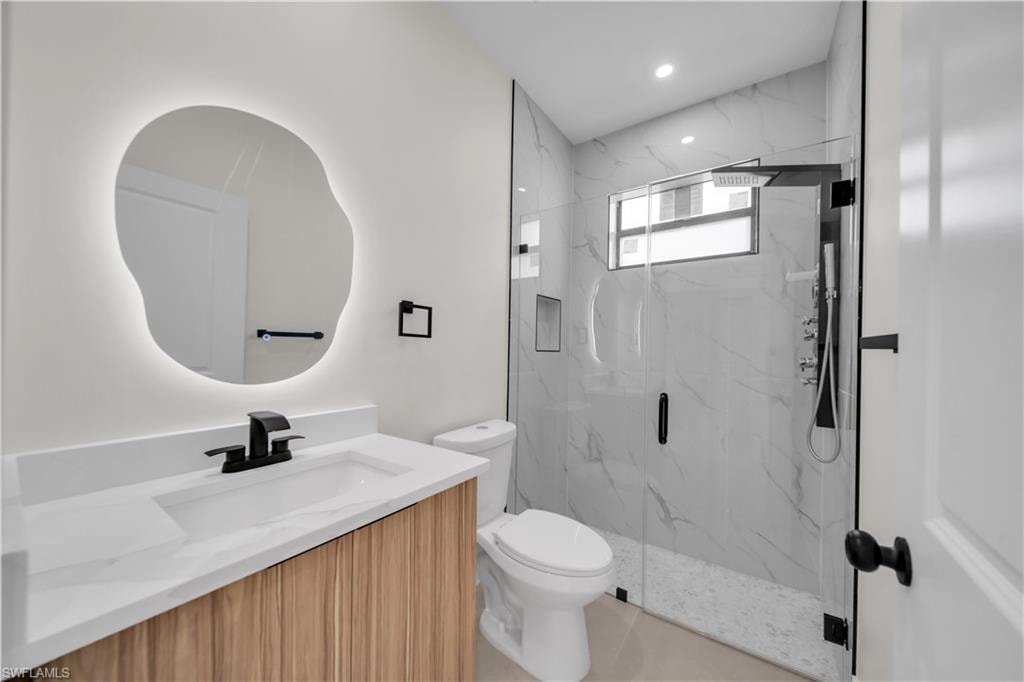Modern bathroom featuring a custom-shaped backlit mirror, wood-finish vanity with a white countertop, and a glass-enclosed shower with large format tile surround