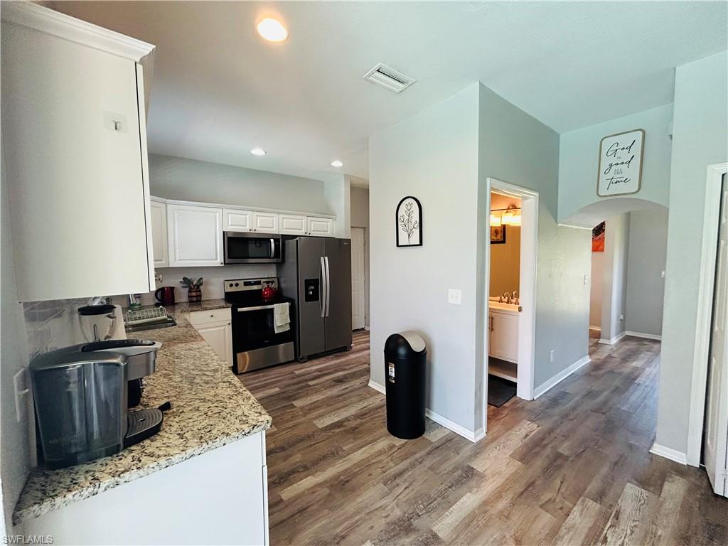 Kitchen featuring white cabinetry, granite countertops, stainless steel appliances, and wood-finish flooring