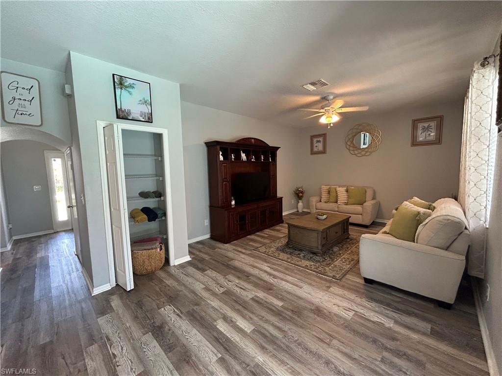 Wood-finish flooring throughout, ceiling fan with integrated lighting, built-in shelving, arched doorway