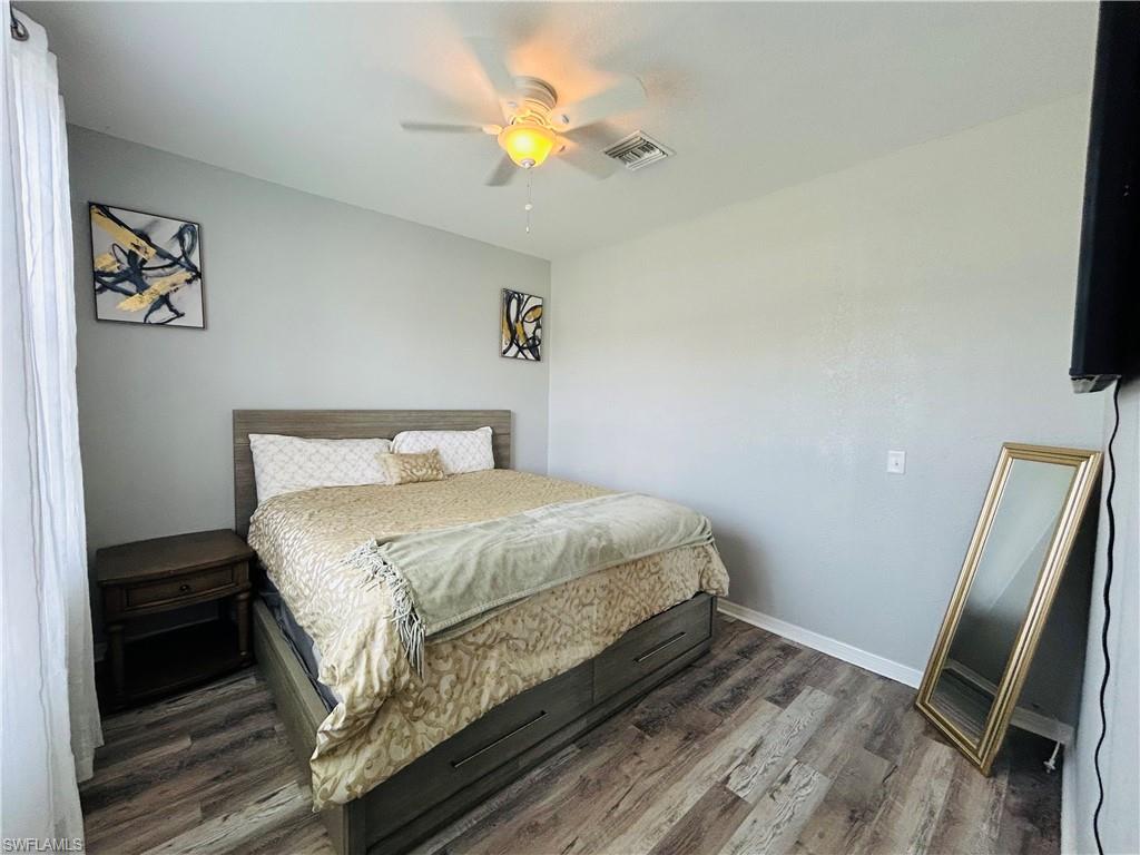 Bright secondary bedroom featuring a wood-finish platform bed frame, wood-look plank flooring, ceiling fan with integrated lighting, and abundant natural light from window with white curtains