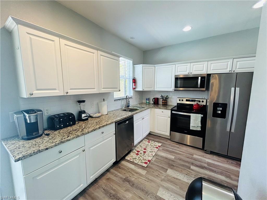 Kitchen featuring white cabinetry, granite countertops, stainless steel appliances, a white subway tile backsplash, and wood-finish flooring
