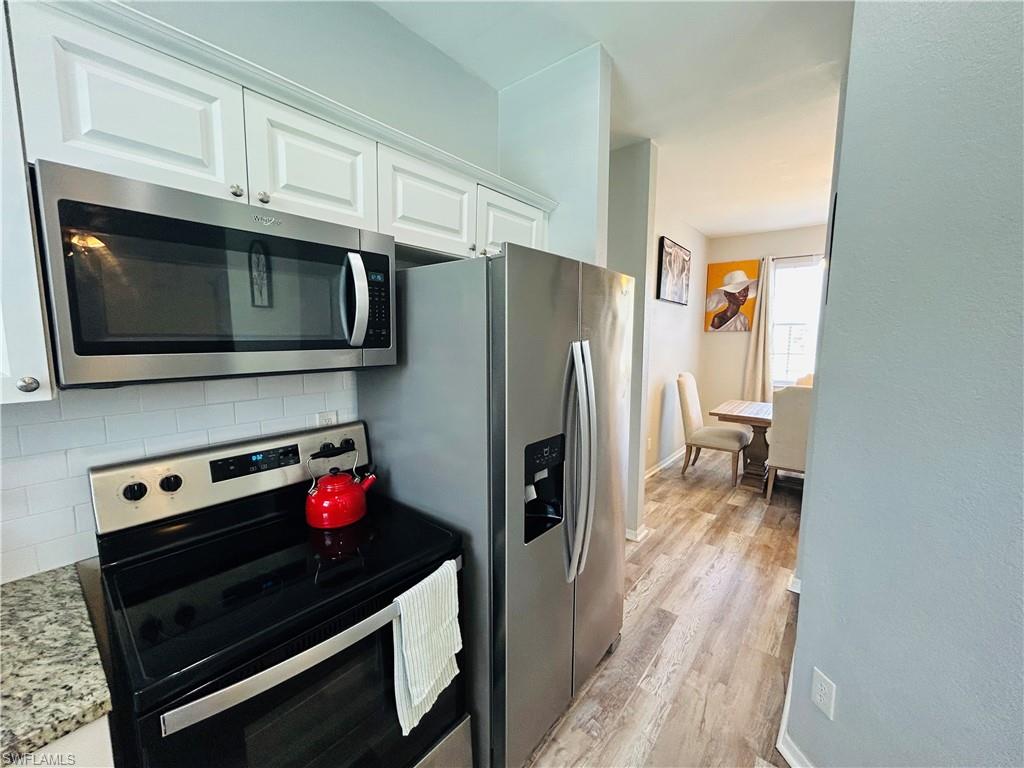 Kitchen featuring stainless steel appliances, white cabinetry, tile backsplash, and wood-finish flooring
