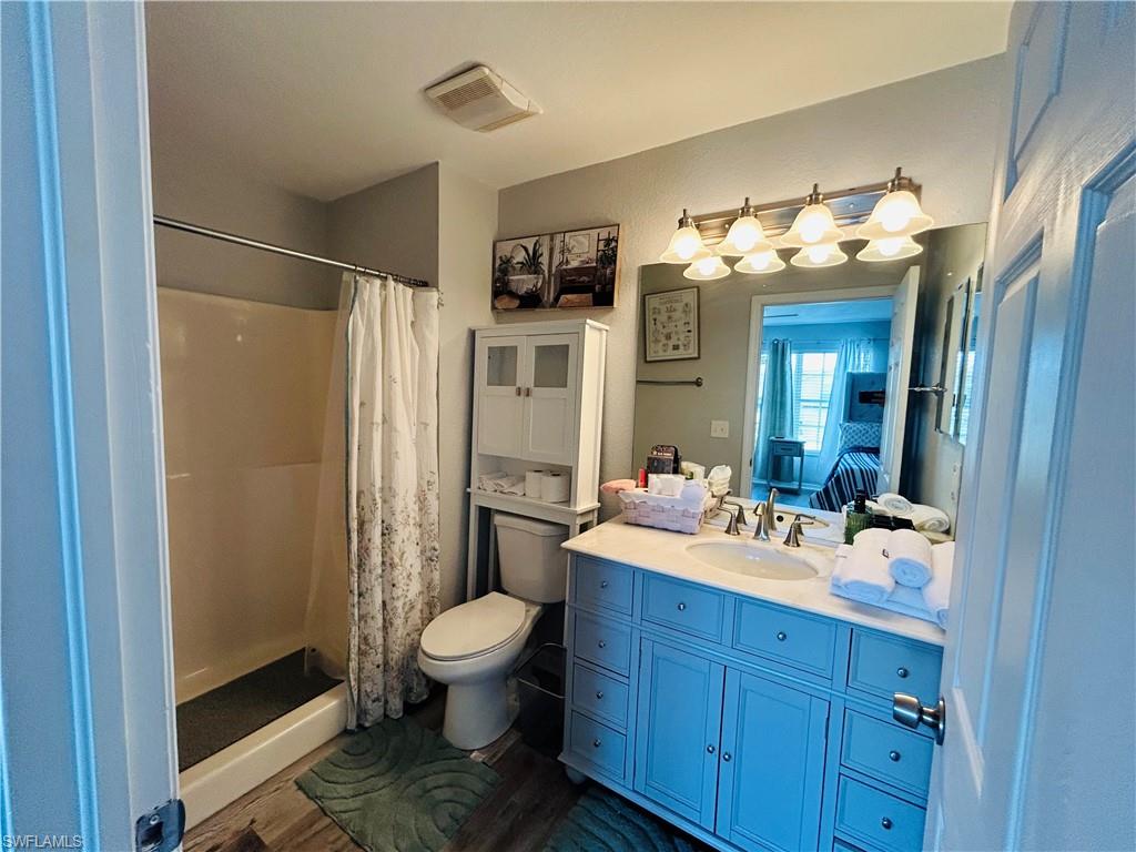 Bathroom featuring a blue vanity with a single basin, a shower-tub combination, wood-finish flooring, and a wall-mounted medicine cabinet