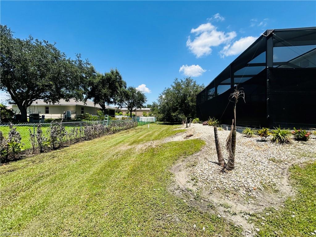 Expansive outdoor area featuring a screened enclosure, mature trees, a chain-link fence, and a gravel landscape bed with plantings