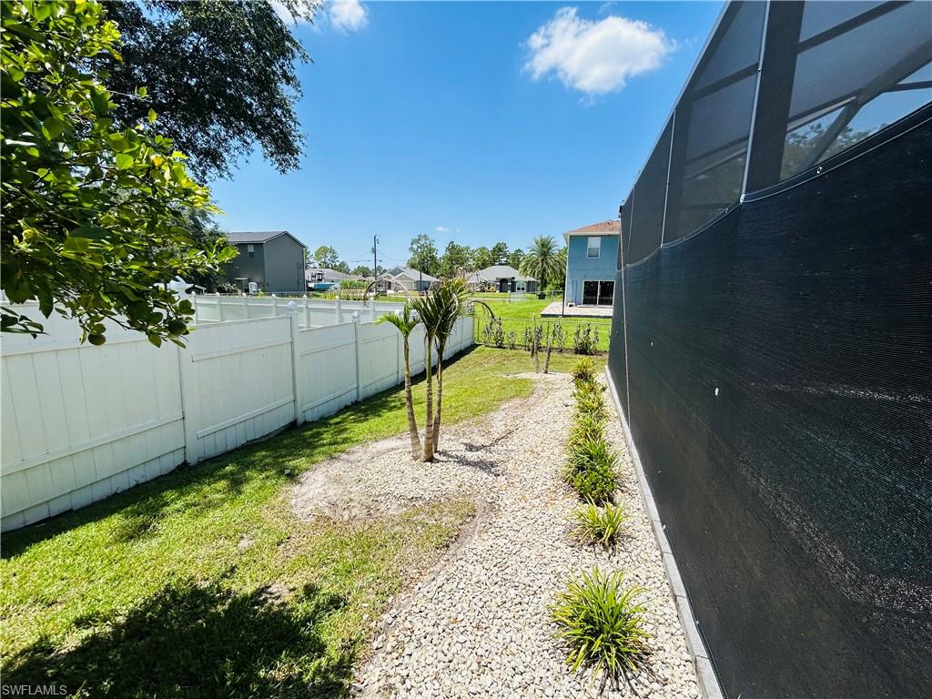 White privacy fencing, landscaped garden beds with decorative rock, and mature plantings