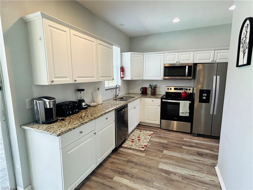 White cabinetry, granite countertops, stainless steel appliances, wood-finish flooring, and recessed lighting