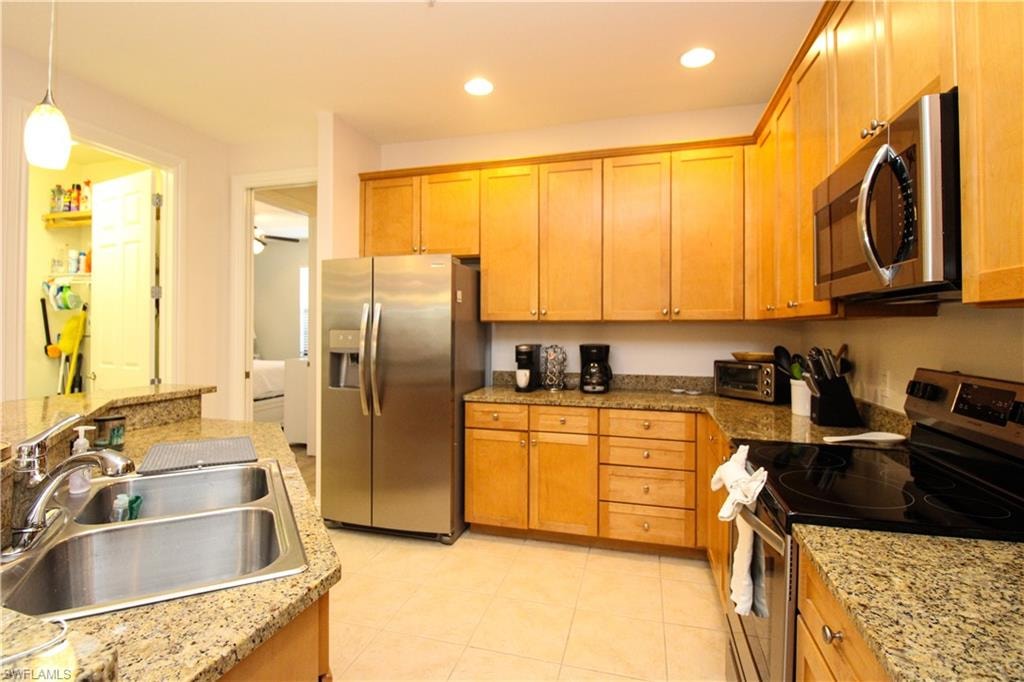Kitchen with light stone countertops, sink, stainless steel appliances, decorative light fixtures, and light tile patterned floors