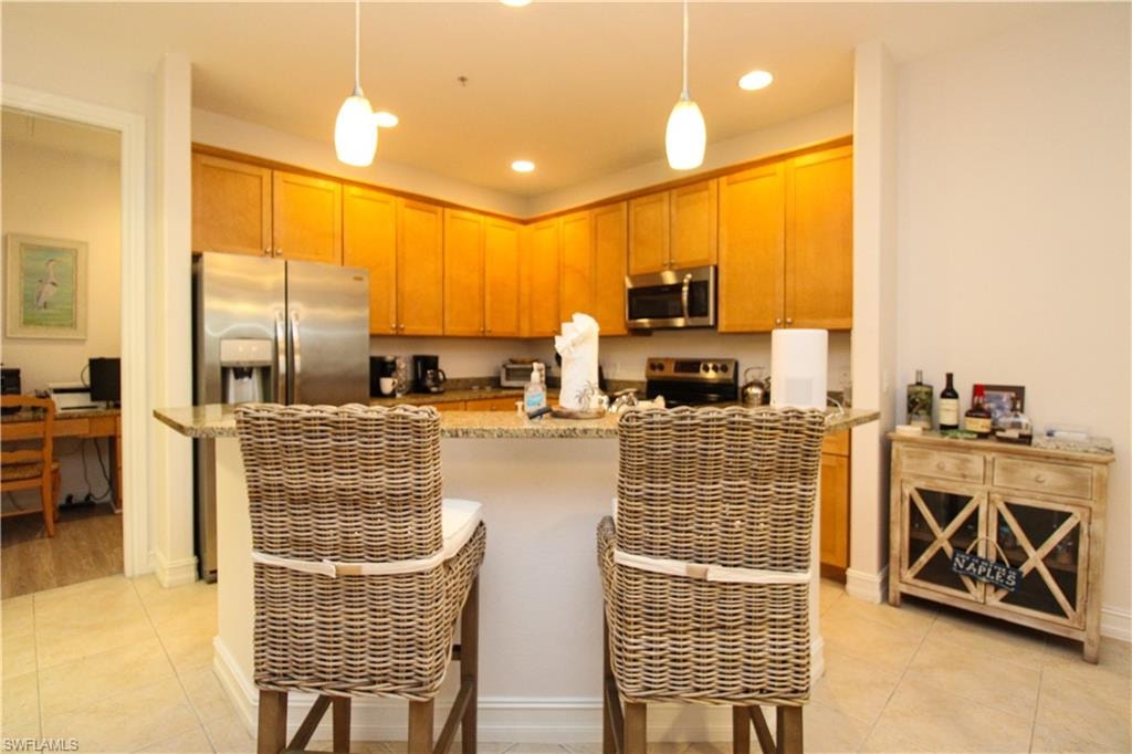 Kitchen featuring light stone countertops, appliances with stainless steel finishes, light tile patterned floors, and hanging light fixtures