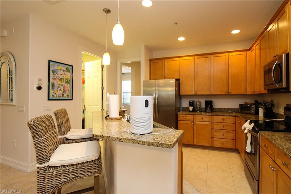 Kitchen featuring light tile patterned floors, light stone countertops, appliances with stainless steel finishes, pendant lighting, and a breakfast bar