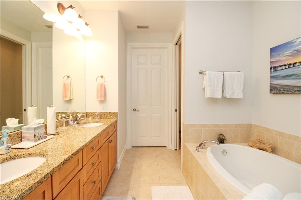 Bathroom featuring vanity, a relaxing tiled tub, and tile patterned floors