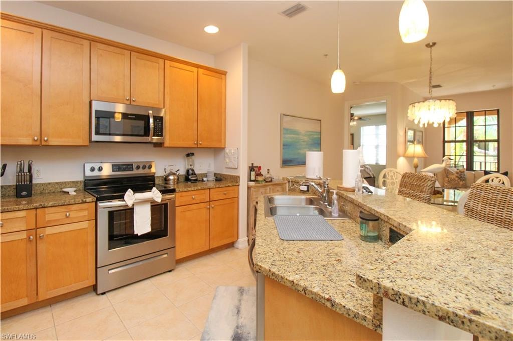 Kitchen with hanging light fixtures, light stone counters, appliances with stainless steel finishes, ceiling fan with notable chandelier, and sink
